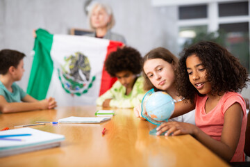 in geography lesson, students carefully listen to woman teacher who talks about Mexicо