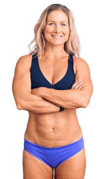 Middle age fit blonde woman wearing bikini happy face smiling with crossed arms looking at the camera. positive person.