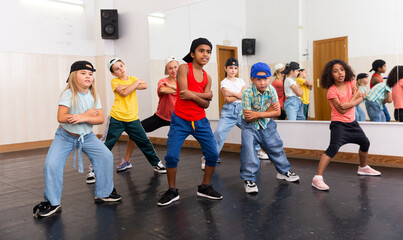 Portrait of cheerful preteen girl practicing dance movements with group of children in choreography class