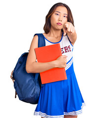 Young beautiful chinese girl wearing cheerleader uniform and student backpack holding binder pointing with finger to the camera and to you, confident gesture looking serious