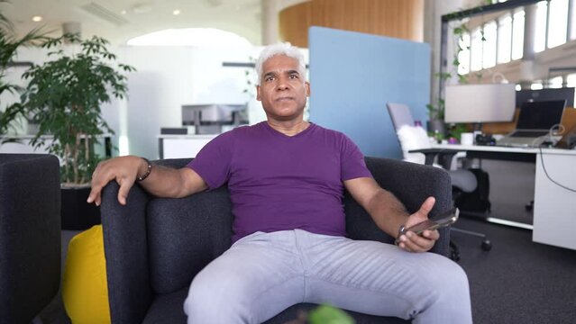 Solid businessman with gray hair sits in a meeting in a modern office, watches a mobile app 