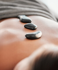 Woman, rocks and back in spa relaxation for treatment, stress relief or massage at resort. Female relaxing with hot stone in physical therapy for skincare, body healing or zen wellness at salon