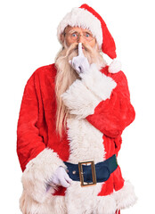 Old senior man with grey hair and long beard wearing traditional santa claus costume asking to be quiet with finger on lips. silence and secret concept.