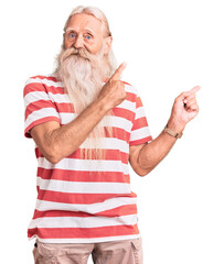 Old senior man with grey hair and long beard wearing striped tshirt smiling and looking at the camera pointing with two hands and fingers to the side.