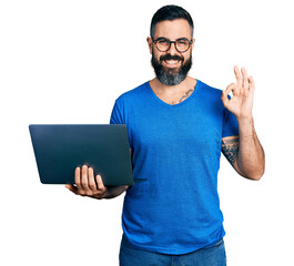 Hispanic man with beard working using computer laptop doing ok sign with fingers, smiling friendly gesturing excellent symbol