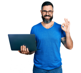 Hispanic man with beard working using computer laptop doing ok sign with fingers, smiling friendly gesturing excellent symbol