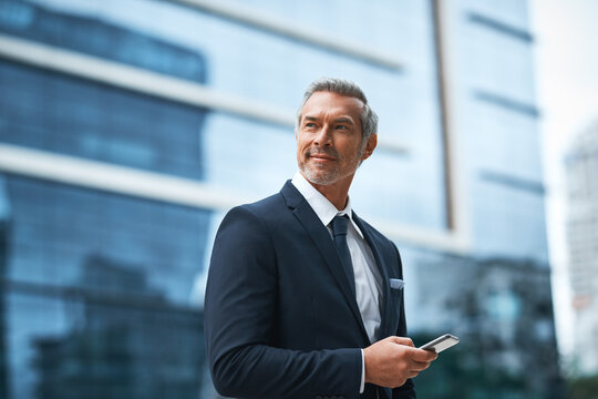 Hard work, determination, persistence creates a boss. Shot of a handsome mature businessman in corporate attire using a cellphone outside outside during the day.