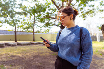 Joven mujer, con mochila, auriculares, usando el celular, telefono. Fotografía plano medio.