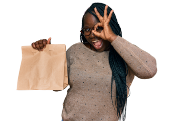Young black woman with braids holding take away paper bag smiling happy doing ok sign with hand on eye looking through fingers