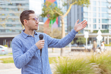 Fototapeta premium Hombre joven, caucásico, de 25 años, con lentes, con un micrófono y camisa azul al aire libre, posible reportero.