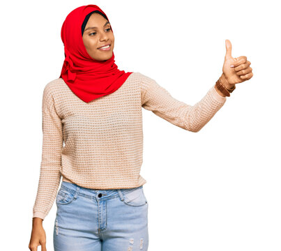 Young african american woman wearing traditional islamic hijab scarf looking proud, smiling doing thumbs up gesture to the side