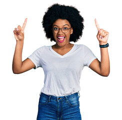 Young african american woman wearing casual white t shirt smiling amazed and surprised and pointing up with fingers and raised arms.