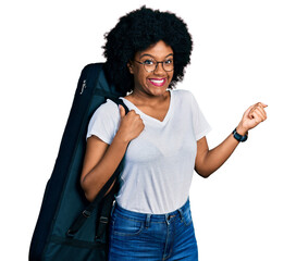 Young african american woman wearing guitar case screaming proud, celebrating victory and success very excited with raised arm