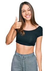 Young brunette woman wearing casual clothes doing happy thumbs up gesture with hand. approving expression looking at the camera showing success.