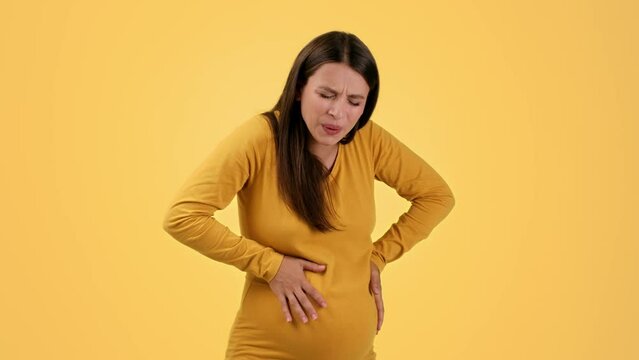 Young unhappy pregnant woman suffering from Braxton Hicks contraction, touching her painful belly, free space