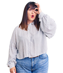 Young plus size woman wearing casual clothes doing ok gesture shocked with surprised face, eye looking through fingers. unbelieving expression.