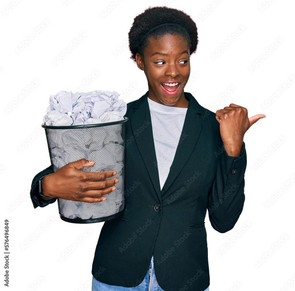 Sticker Young african american girl holding paper bin full of crumpled papers pointing thumb up to the side smiling happy with open mouth