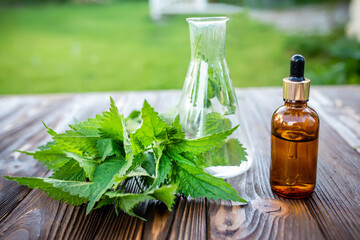 Fresh nettle and a pharmacist tube on a wooden table. Production of cosmetics and products for scalp and hair from nettle.