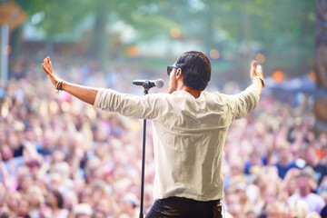 Charismatic frontman. A singer performing on stage at an outdoor music festival.