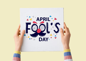 Female hands holding poster with text APRIL FOOLS DAY on beige background