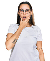Young hispanic woman wearing casual white t shirt looking fascinated with disbelief, surprise and amazed expression with hands on chin