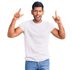 Young latin man wearing casual clothes smiling amazed and surprised and pointing up with fingers and raised arms.