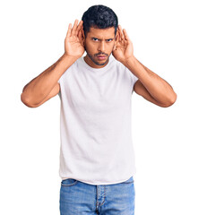 Fototapeta premium Young latin man wearing casual clothes trying to hear both hands on ear gesture, curious for gossip. hearing problem, deaf