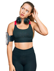 Beautiful blonde woman wearing gym clothes and using headphones confuse and wondering about question. uncertain with doubt, thinking with hand on head. pensive concept.