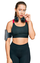 Beautiful blonde woman wearing gym clothes and using headphones mouth and lips shut as zip with fingers. secret and silent, taboo talking