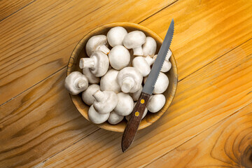 Fresh white mushrooms champignon in brown wooden bowl on wood table background