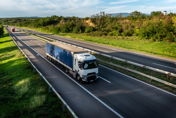 White truck driving on the highway winding through forested landscape in autumn colors at sunset