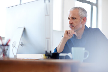 Focussed on insightful solution finding. Low angle view of a mature professional man looking intently at his pc.