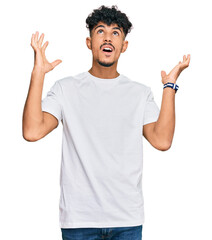 Young arab man wearing casual white t shirt crazy and mad shouting and yelling with aggressive...