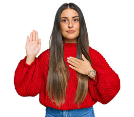 Beautiful hispanic woman wearing casual clothes swearing with hand on chest and open palm, making a...