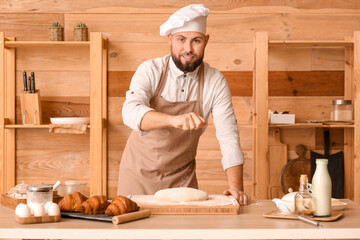 Male baker sprinkling dough with flour at table in kitchen
