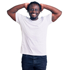 Young african american man with braids wearing casual white tshirt relaxing and stretching, arms and hands behind head and neck smiling happy