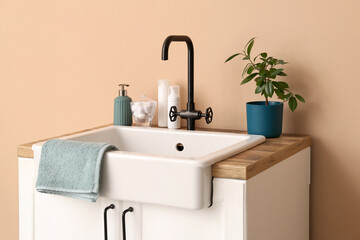 Obraz na płótnie Canvas Table with sink, bath accessories and houseplant near beige wall