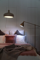 Interior of bedroom with blankets on bed and glowing lamps at night
