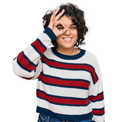 Young hispanic woman with curly hair wearing casual clothes doing ok gesture with hand smiling, eye looking through fingers with happy face.