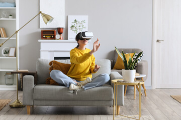 Pretty young woman in VR glasses sitting in sofa at home