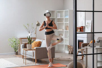Sporty young woman in VR glasses  practising yoga at home