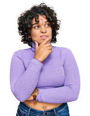 Fototapeta na wymiar Young hispanic woman with curly hair wearing casual clothes thinking worried about a question, concerned and nervous with hand on chin