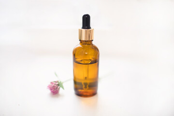 Cosmetic bottle made of dark glass with a dispenser on a white background with fresh clover. Production of essential oil for cosmetology