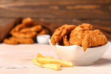 Bowl of tasty nuggets and french fries on light wooden table