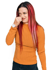 Young caucasian woman wearing casual clothes smelling something stinky and disgusting, intolerable smell, holding breath with fingers on nose. bad smell - obrazy, fototapety, plakaty