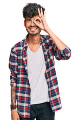 Young hispanic man wearing casual clothes doing ok gesture with hand smiling, eye looking through fingers with happy face.