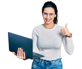 Young hispanic woman working using computer laptop smiling happy and positive, thumb up doing excellent and approval sign
