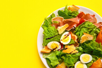 Plate of delicious salad with boiled eggs and jamon on yellow background