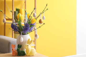 Vase with flowers, tree branches, Easter eggs and rabbits on table in living room