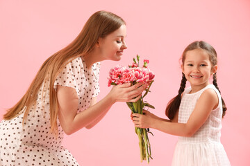 Cute little girl greeting her mother with flowers on pink background